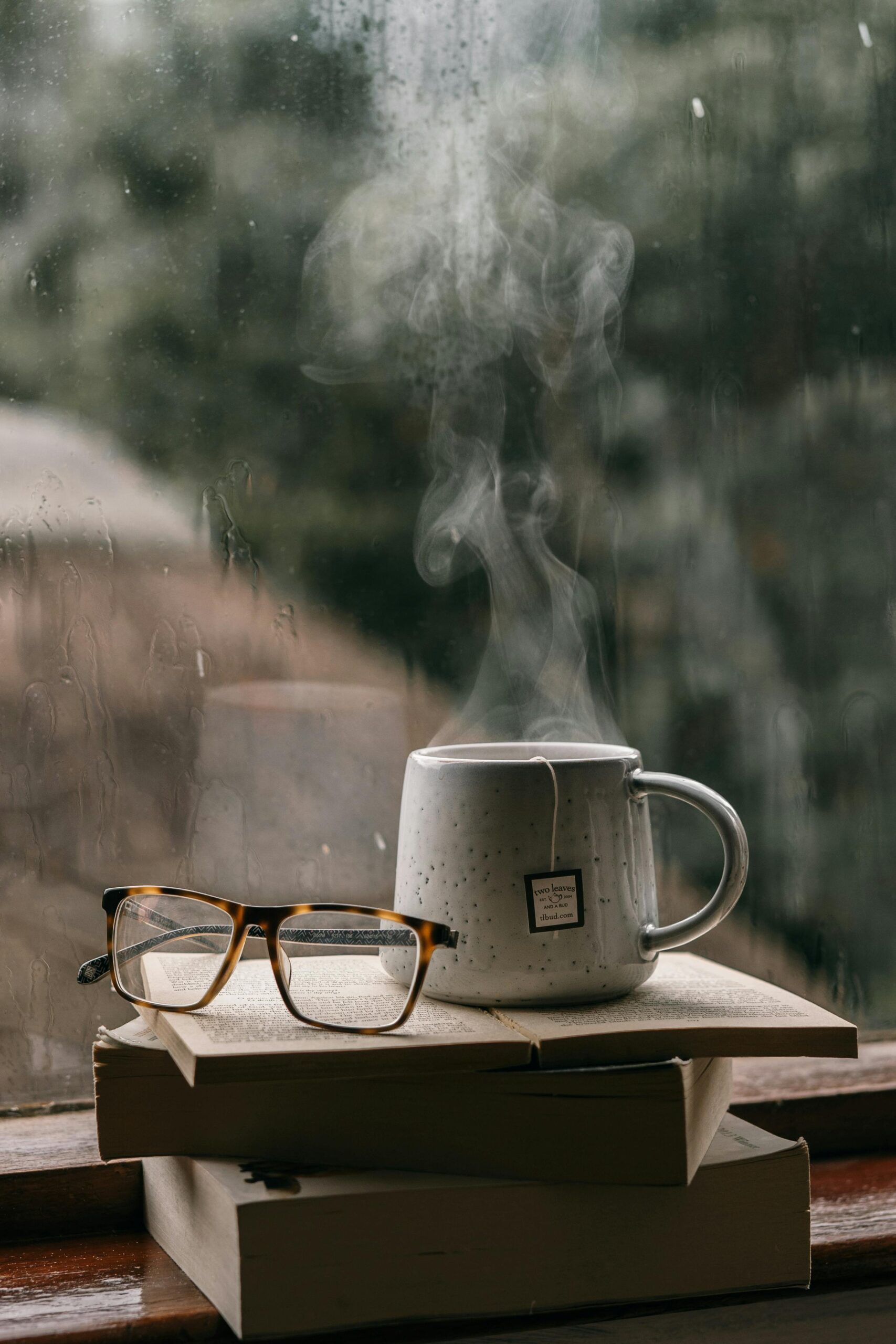 Cup of Tea and an Eyeglasses on the Stacks of Books Near the Window